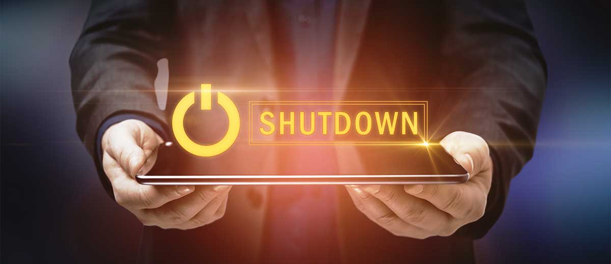 Imagen de una persona sosteniendo una laptop cerrada con la palabra "Shut Down" flotando sobre ella.